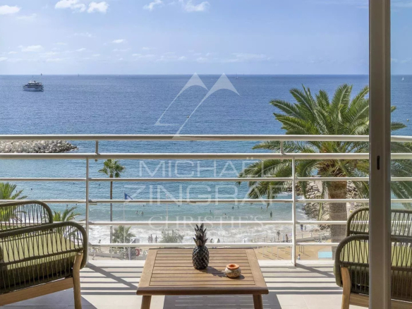 Vue panoramique sur la mer depuis un balcon avec des chaises et une table en bois.