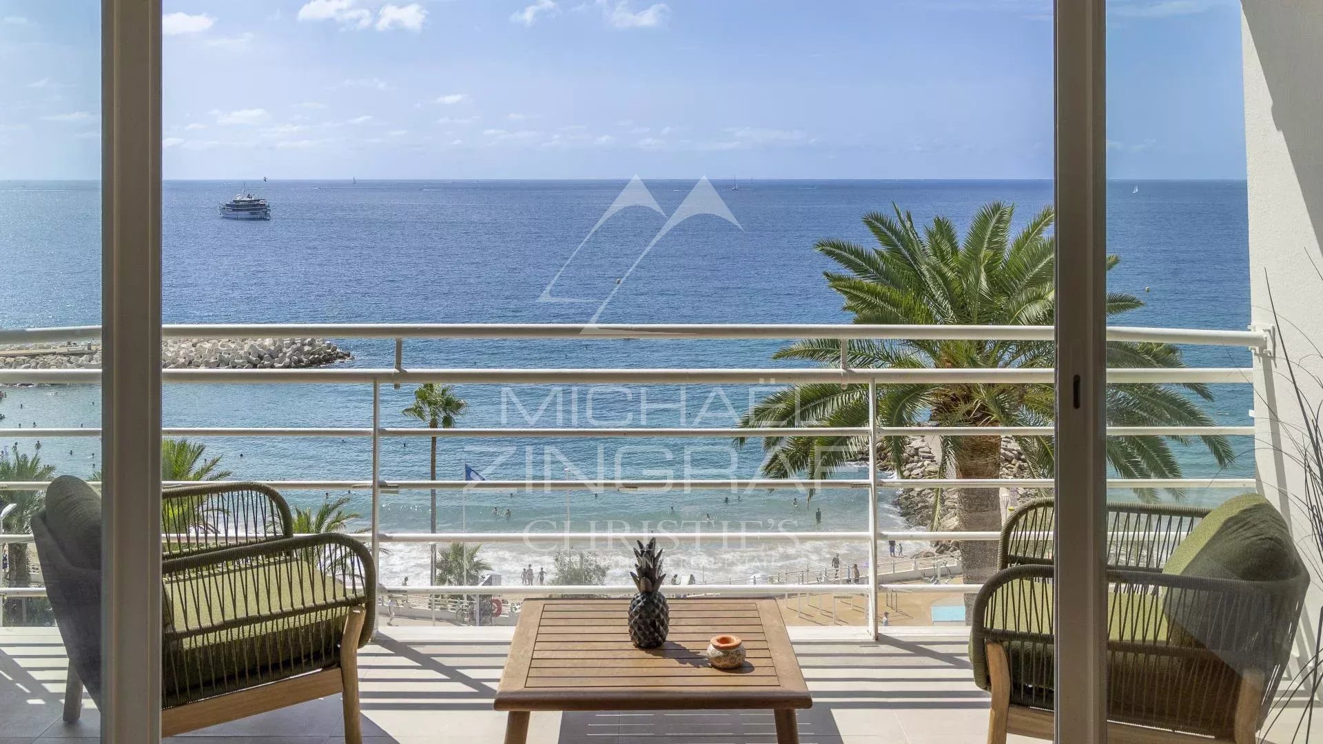 Vue panoramique sur la mer depuis un balcon avec des chaises et une table en bois.