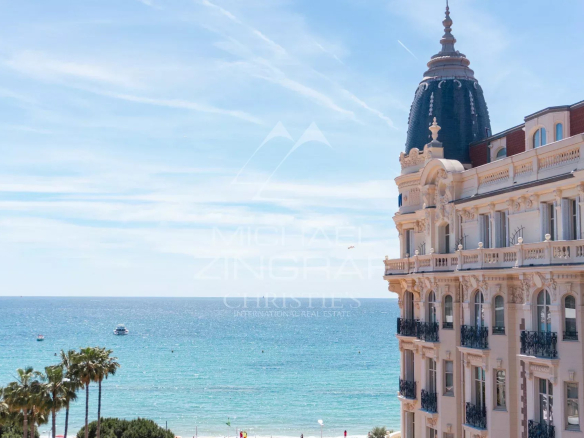 View of the sea and a building in Cannes, with palm trees in the foreground.