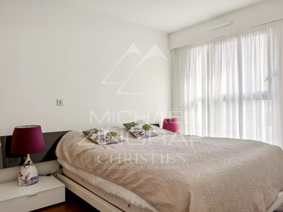 Chambre d'un appartement 2 pièces à Cannes, avec lit double et fenêtres laissant entrer la lumière.