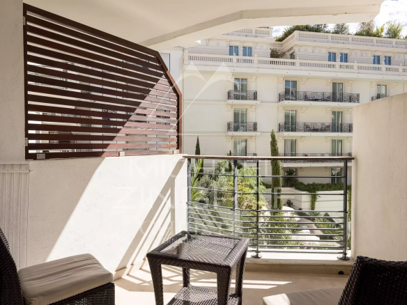Terrasse d'un appartement à Cannes avec mobilier de jardin et vue sur un bâtiment adjacent.