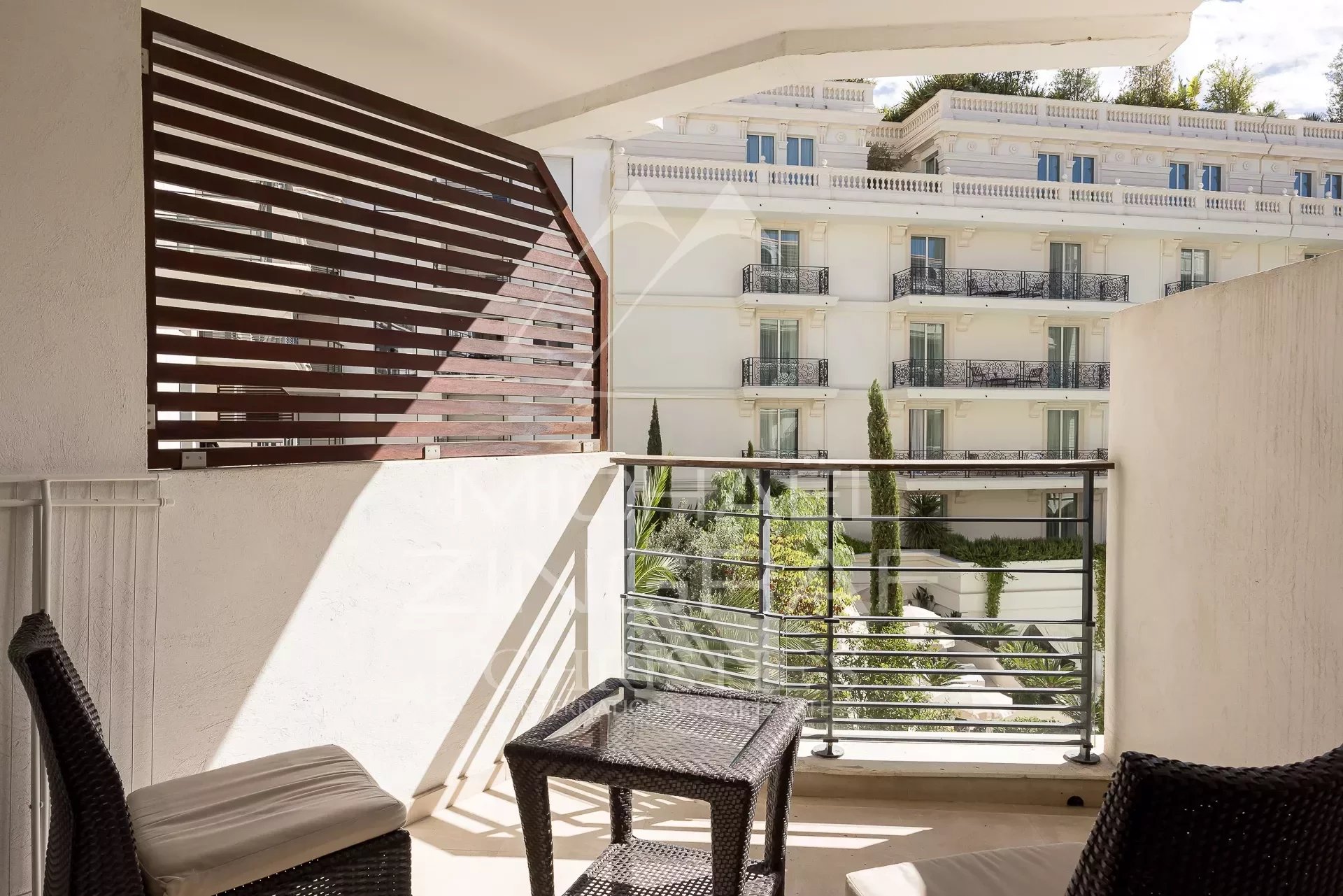 Terrasse d’appartement à Cannes Terrasse d'un appartement à Cannes avec mobilier de jardin et vue sur un bâtiment adjacent.