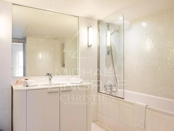 Modern bathroom with bathtub and shower, light tiles and illuminated mirror.