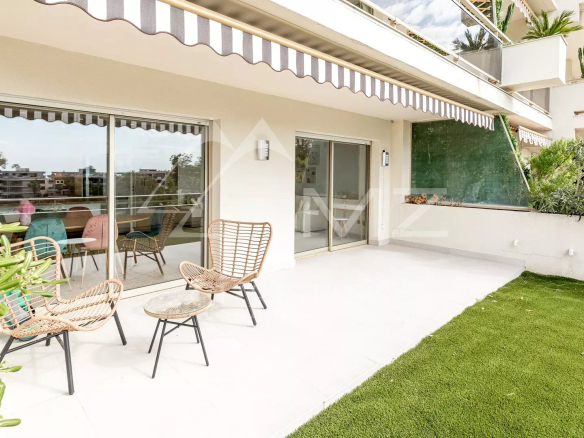 Terrasse spacieuse d'un appartement à Cannes avec vue sur la mer, mobilier extérieur et verdure.