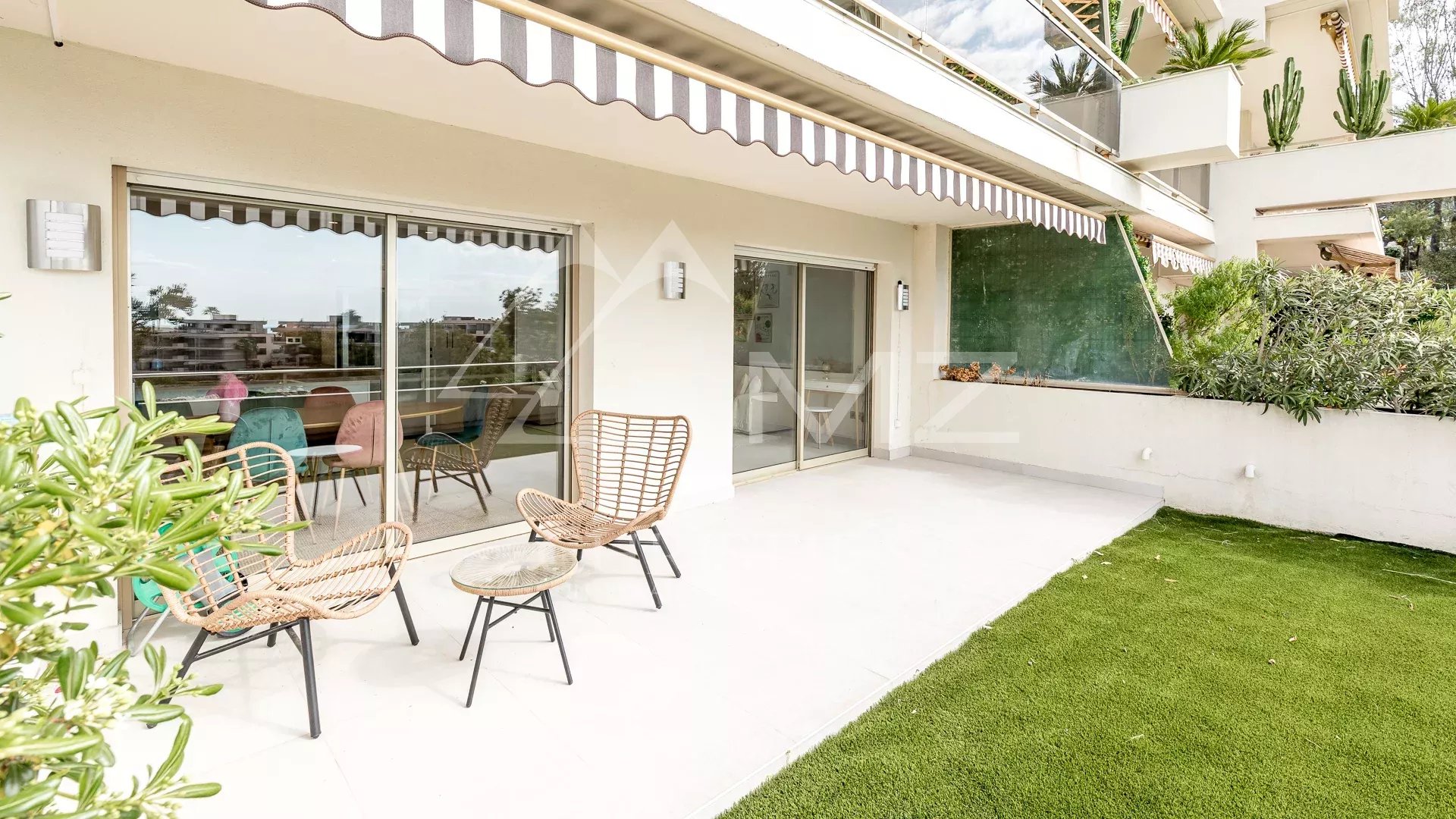 Terrasse spacieuse d'un appartement à Cannes avec vue sur la mer, mobilier extérieur et verdure.