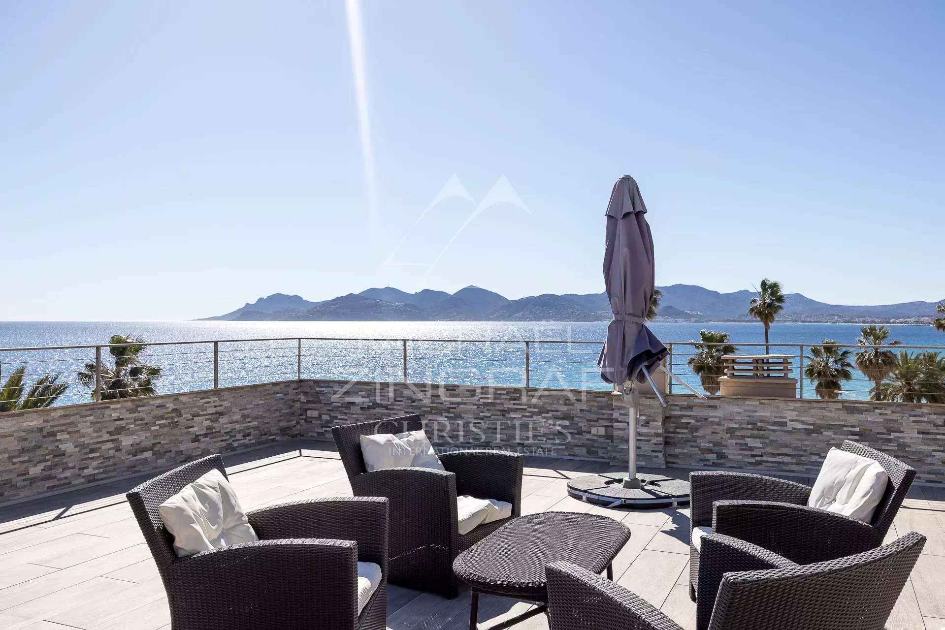 Penthouse with sea view in Cannes Rooftop terrace of a penthouse with sea views in Cannes, rattan armchairs and parasol.