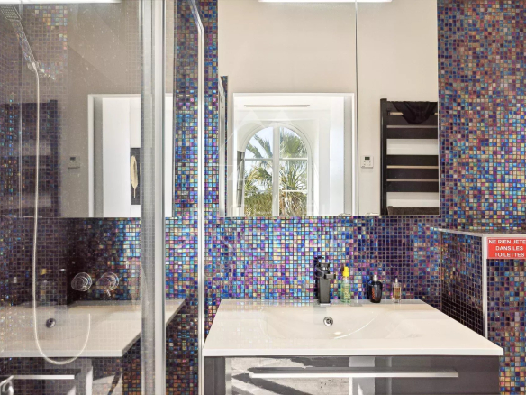 Salle de bain moderne avec carrelage coloré et miroir, vue sur une fenêtre avec palmier.