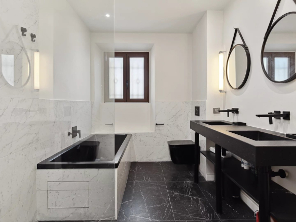 Modern bathroom with bathtub, double sinks and mirror, decorated in marble and black.