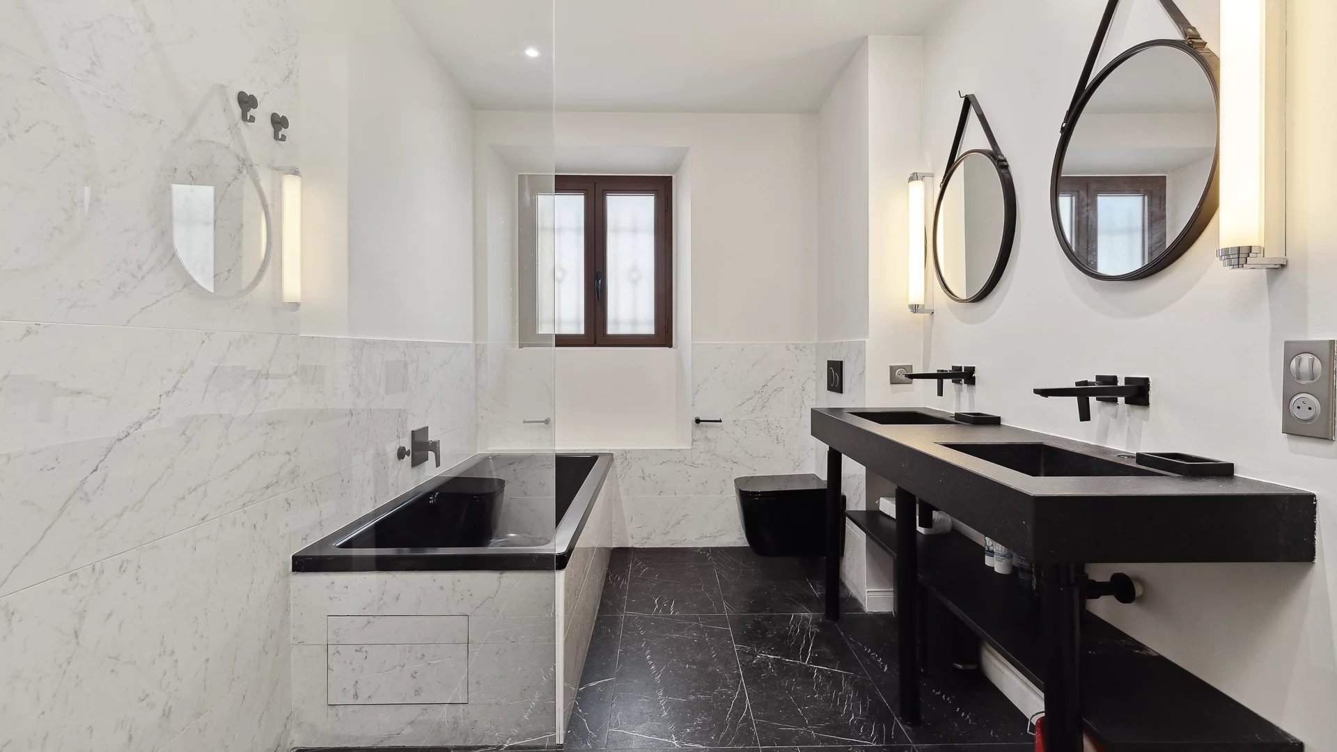 Elegant bathroom in Cannes Modern bathroom with bathtub, double sinks and mirror, decorated in marble and black.