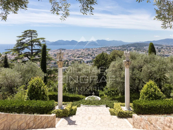 Vue panoramique sur la baie de Cannes depuis un jardin paysager avec des colonnes en pierre.