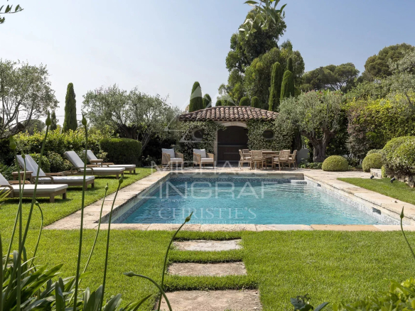 Piscine entourée de chaises longues et jardin paysager dans une villa à Cannes-Californie.