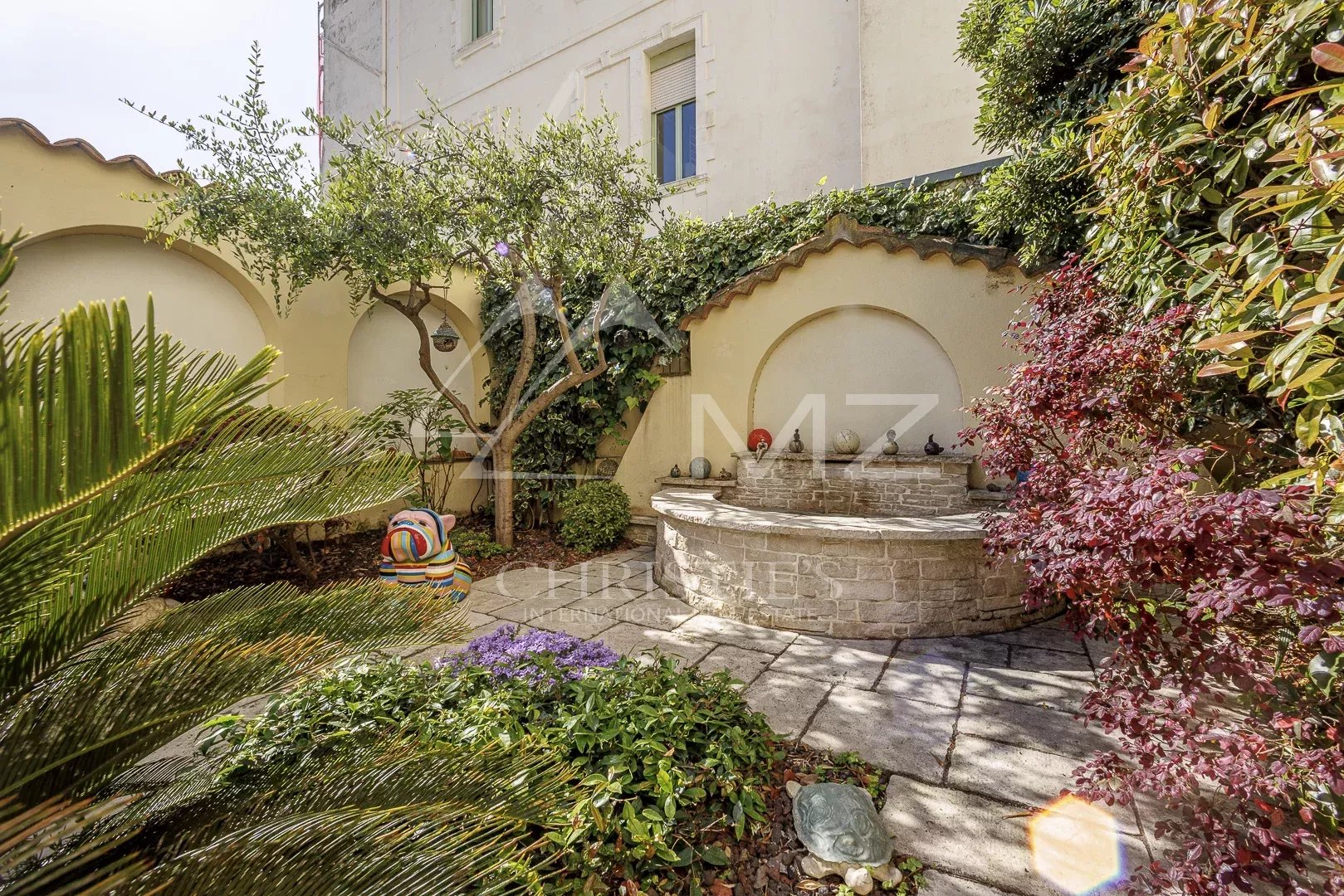 Jardin d'une maison de pécheurs avec fontaine et végétation à Cannes Palm Beach.