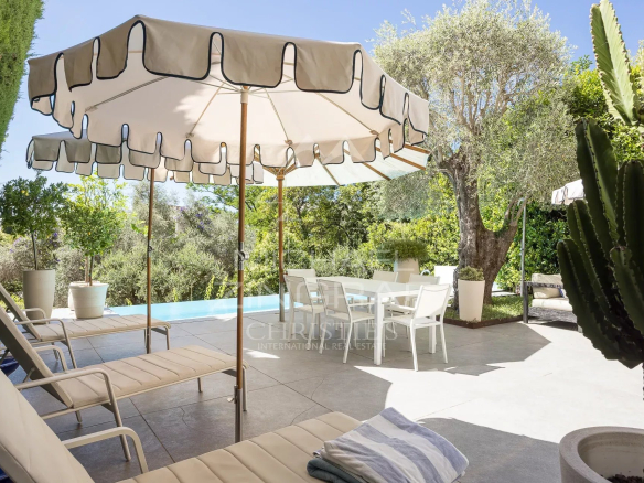 Terrasse avec chaises longues et parasol, piscine et jardin verdoyant.