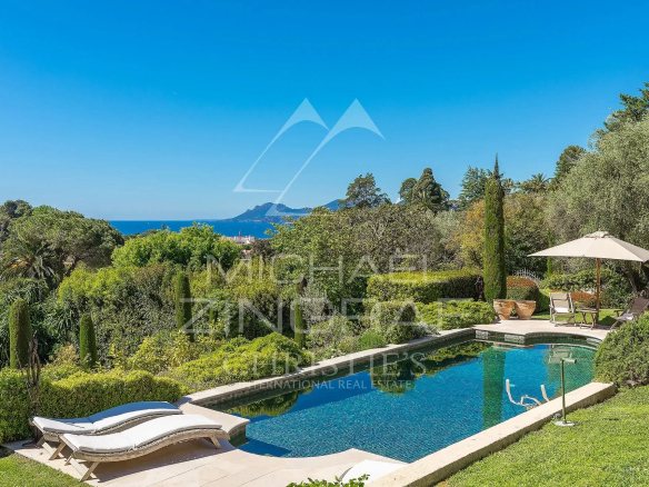 Vue sur une piscine et un jardin paysager avec la baie de Cannes en arrière-plan.