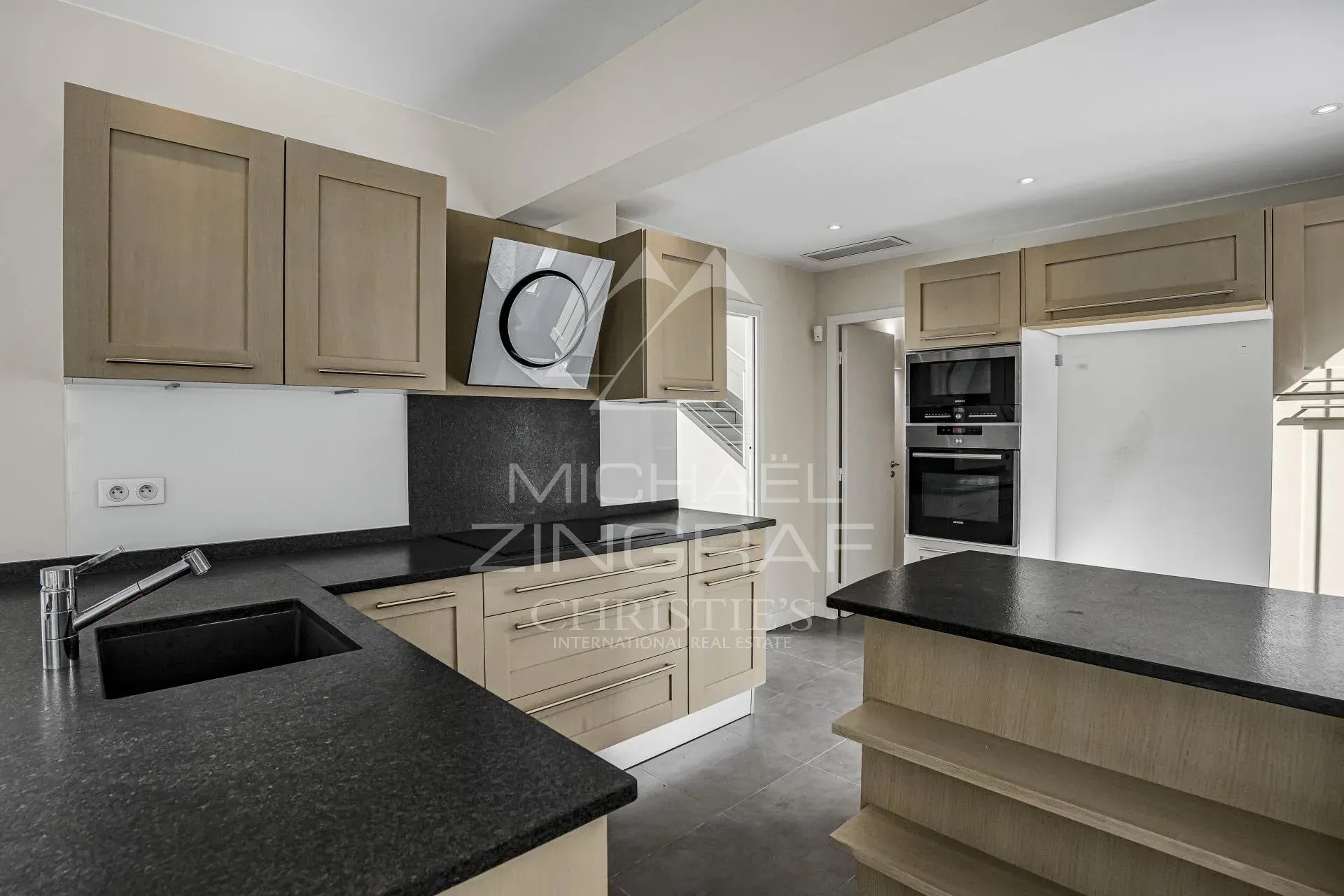 Cuisine de villa à Cannes Cuisine moderne dans une villa à Cannes, avec des meubles en bois clair et un plan de travail en granit.