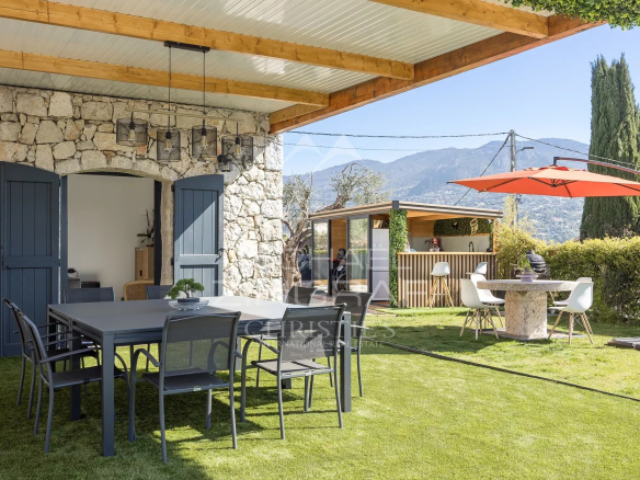 Stone wall house with blue doors opening to a covered patio and a large outdoor dining table on the lawn