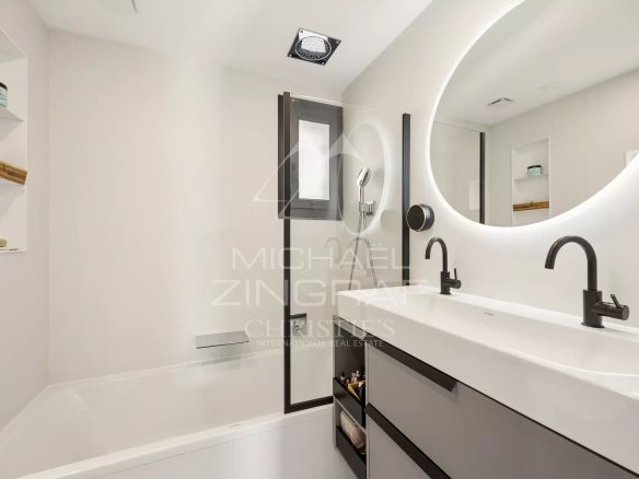 Modern white bathroom with a double sink, black faucets, and an illuminated round mirror above a grey vanity.