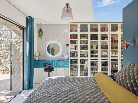 Bedroom with glass-front shoe cabinet, teal desk, round mirror and sliding door opening to a stone patio outside.