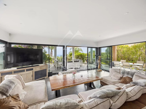 Intérieur d'une villa contemporaine avec salon spacieux et grandes baies vitrées donnant sur l'extérieur.