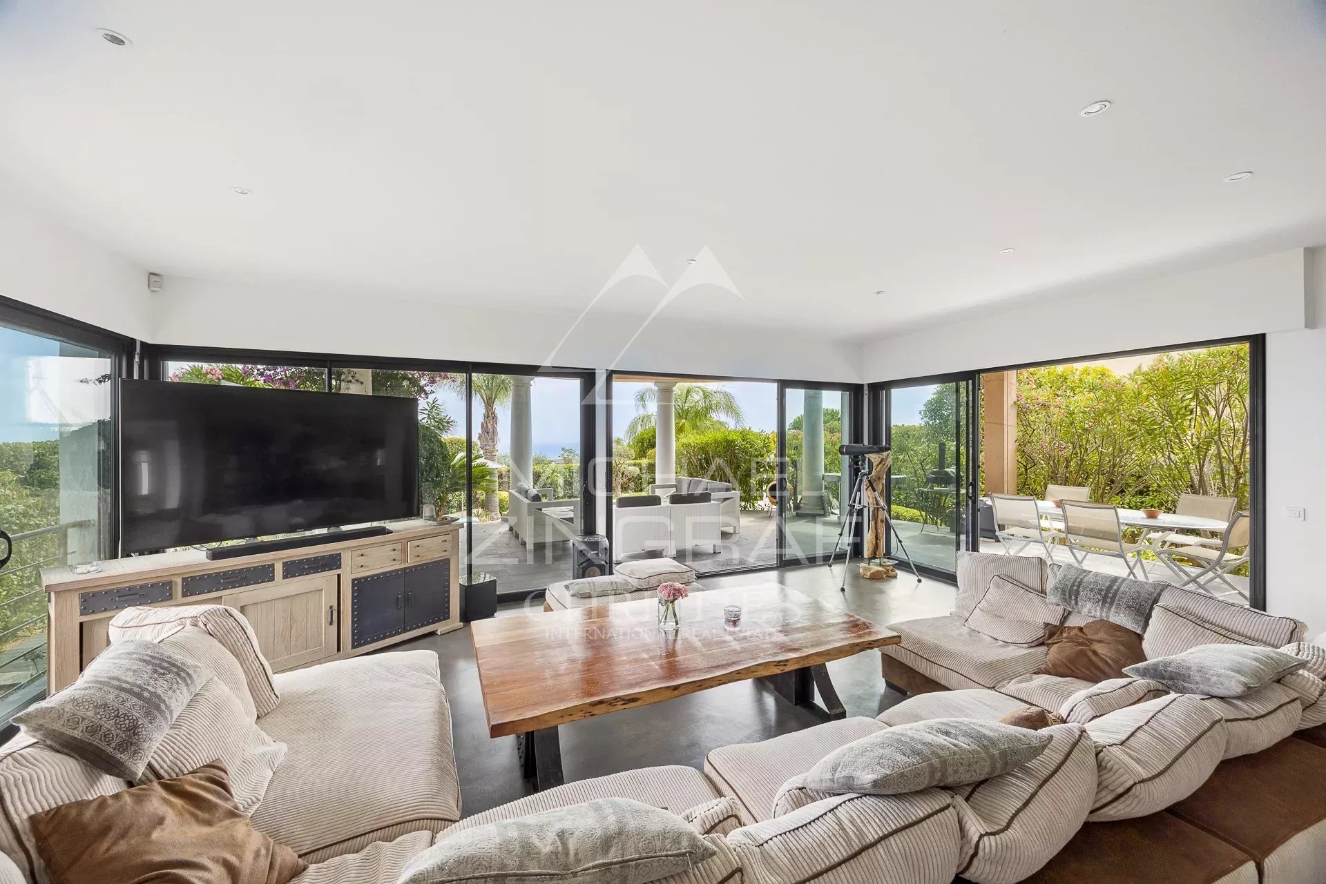 Intérieur d'une villa contemporaine avec salon spacieux et grandes baies vitrées donnant sur l'extérieur.