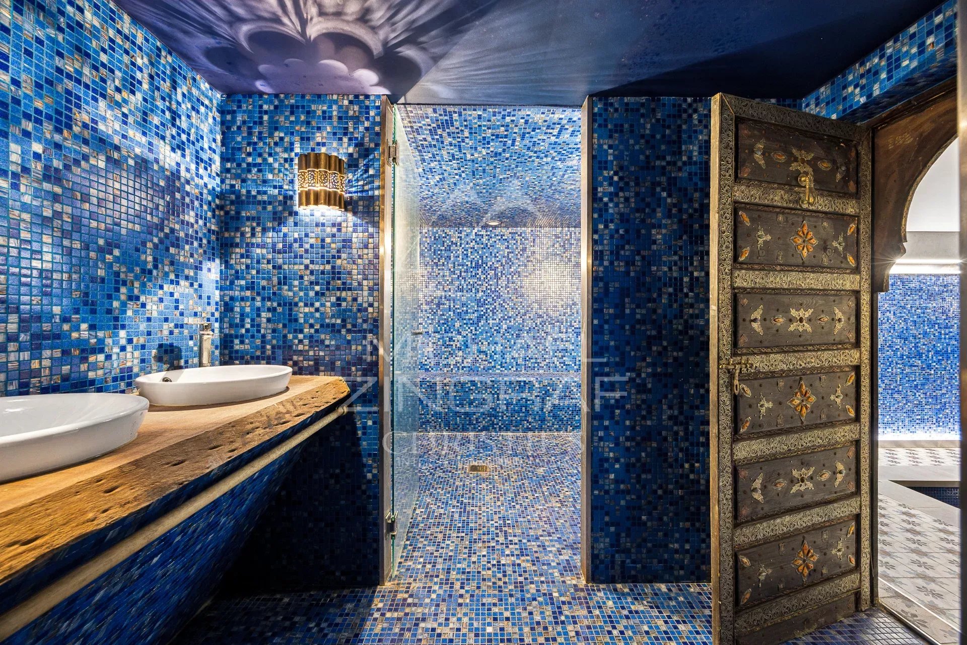 Salle de bains moderne avec carrelage bleu et douche en verre, décorée de bois et de métal.