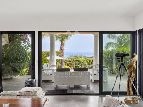 Vue intérieure d'une villa contemporaine avec accès à une terrasse et vue sur la mer.