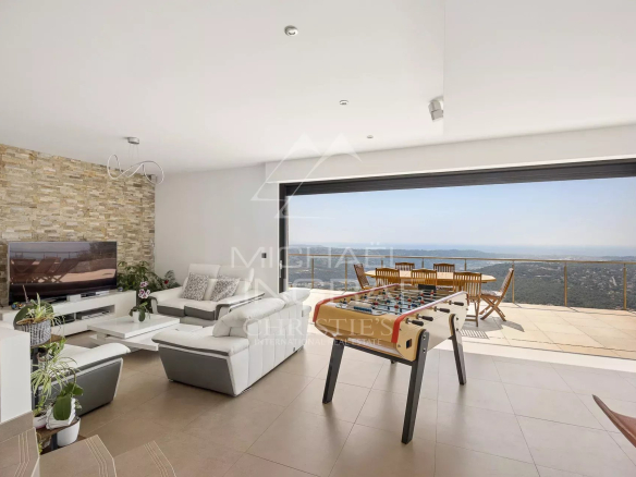 Intérieur d'une villa moderne avec vue panoramique sur la mer, salon lumineux et espace de vie ouvert.
