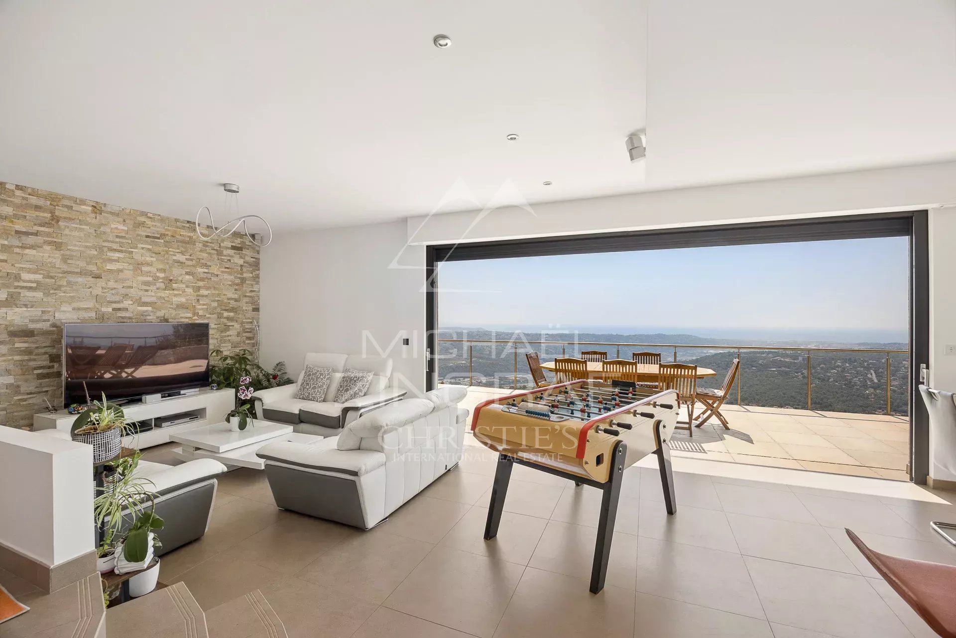 Intérieur d'une villa moderne avec vue panoramique sur la mer, salon lumineux et espace de vie ouvert.