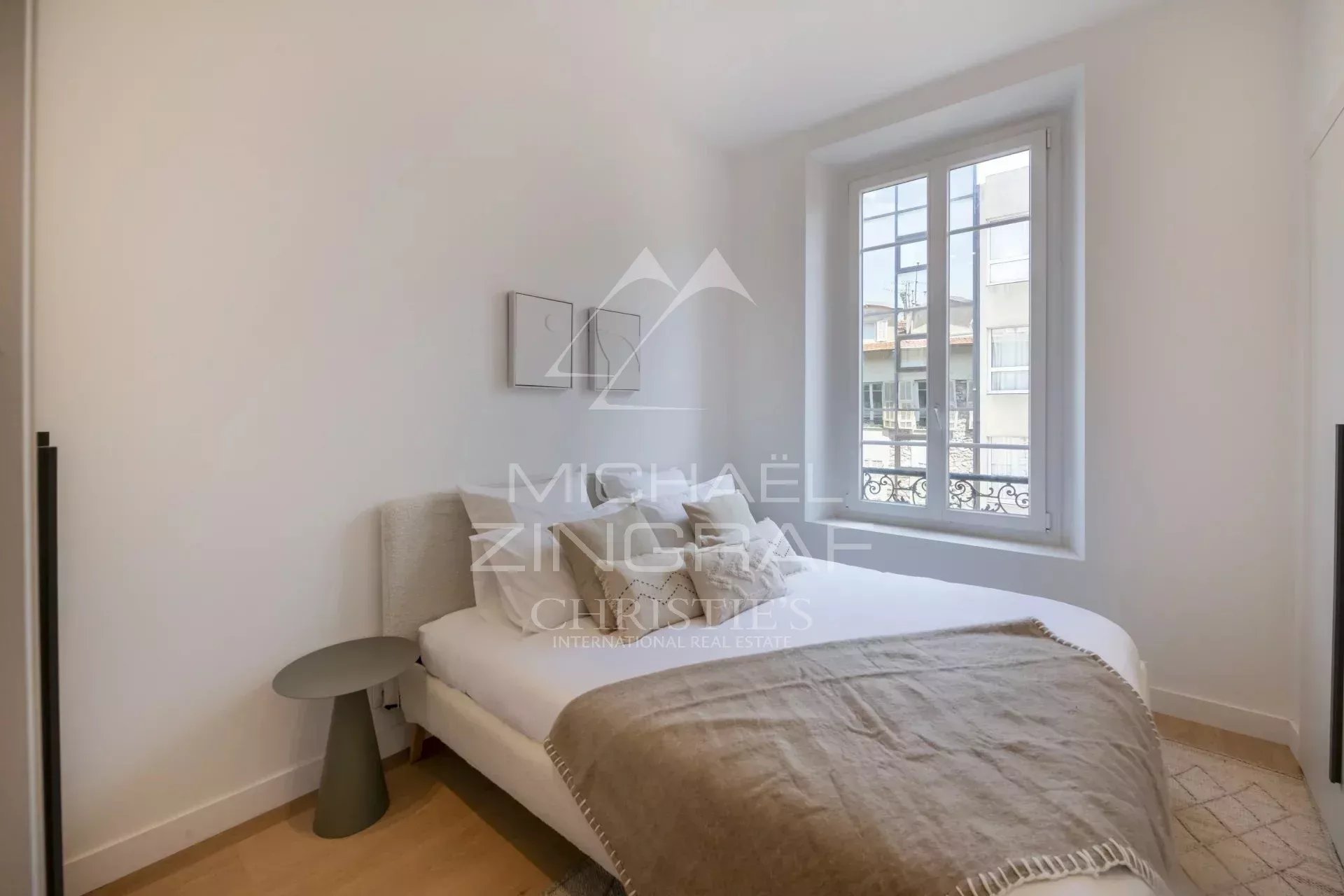 Chambre d'un appartement rénové avec lit double et fenêtre donnant sur la rue à Nice.