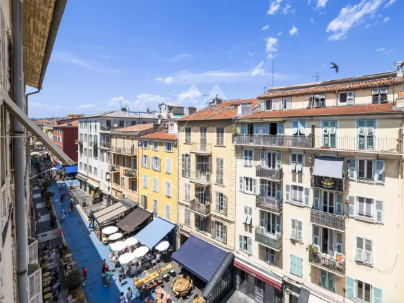 Vue sur des immeubles colorés et une rue animée à Nice, avec des terrasses de café.