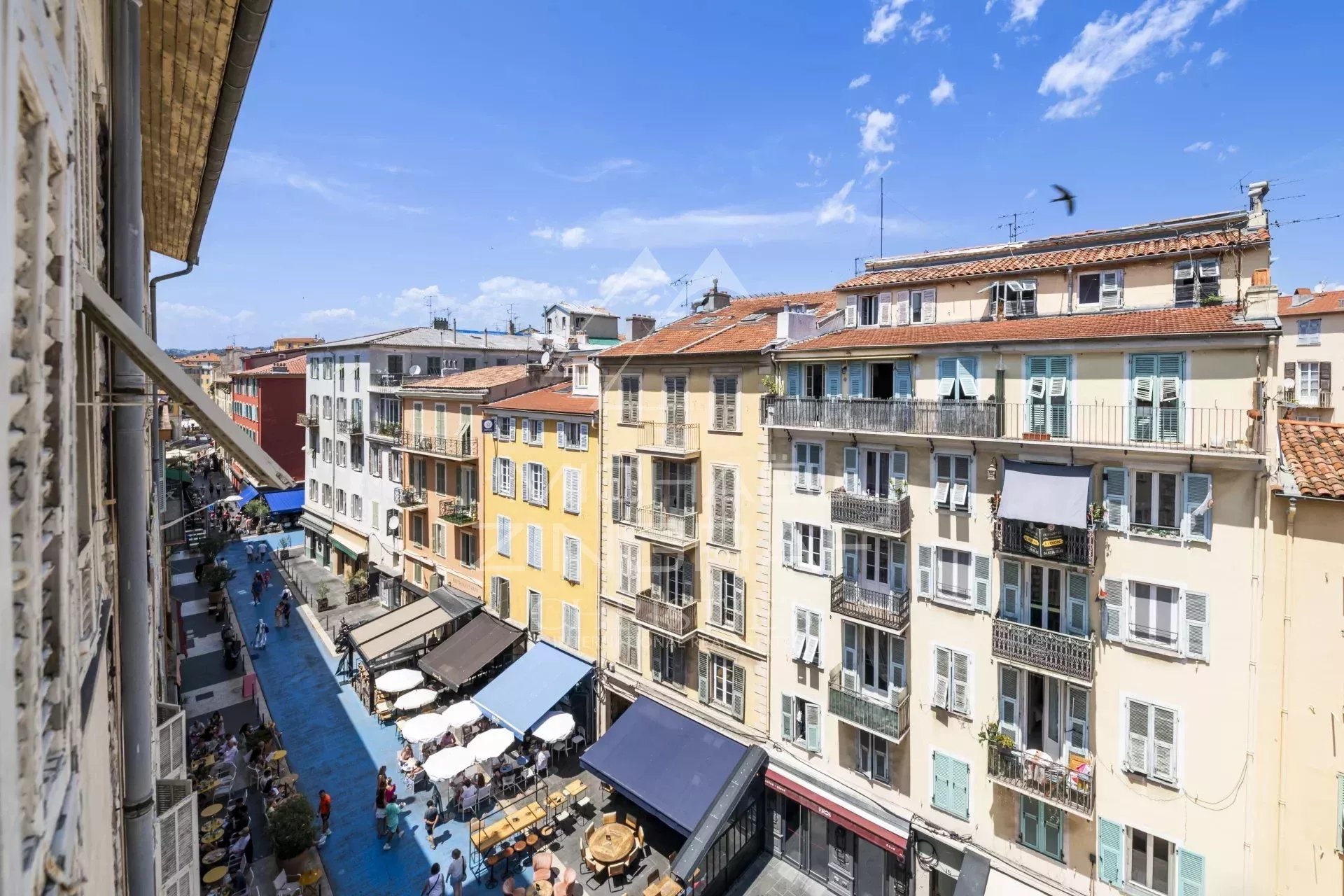 Vue sur des immeubles colorés et une rue animée à Nice, avec des terrasses de café.