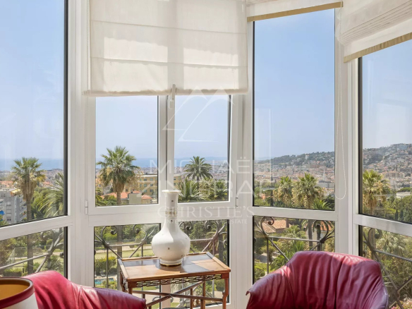 Vue depuis un appartement à Nice avec des fenêtres panoramiques et des fauteuils rouges.