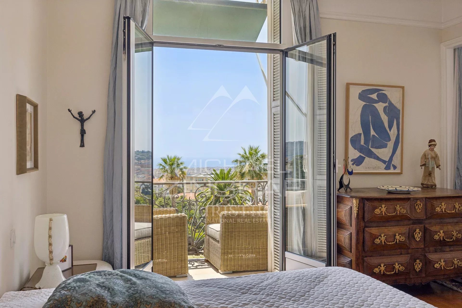 Chambre d'un appartement avec vue sur la mer à Nice, fenêtres ouvertes sur un balcon.