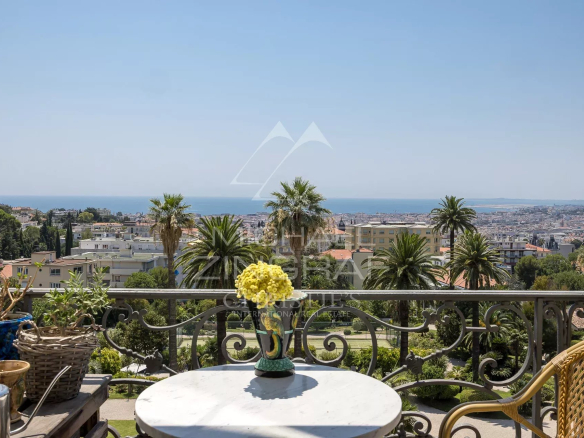 Vue depuis un balcon d'un appartement à Nice, avec mer et jardins en arrière-plan.