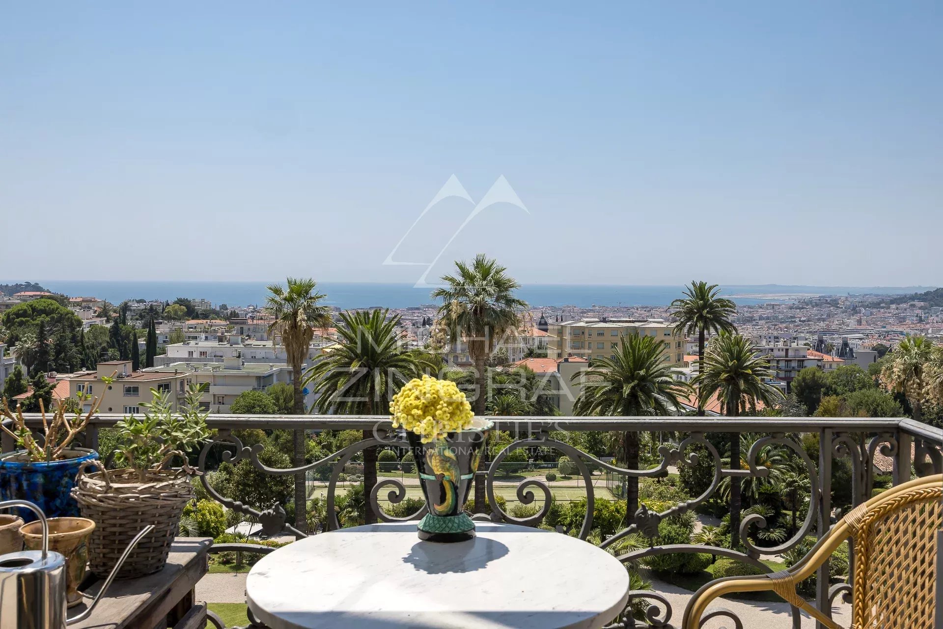Vue depuis un balcon d'un appartement à Nice, avec mer et jardins en arrière-plan.
