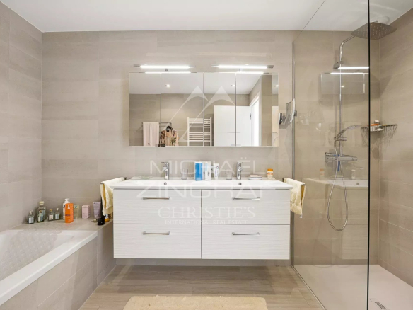 Salle de bain moderne avec baignoire et douche, décor beige, miroir et rangements.