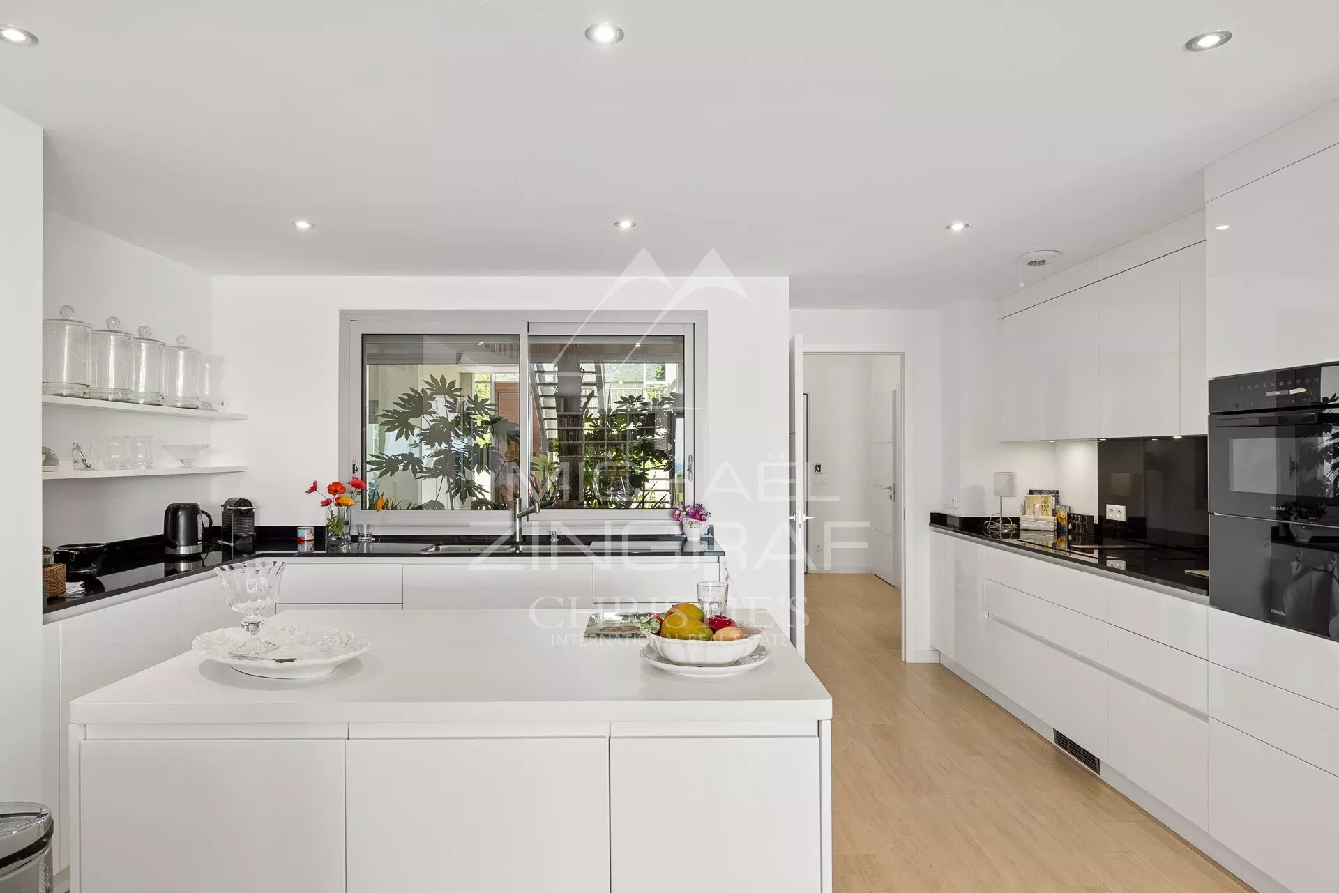Cuisine d’un appartement d’exception à Nice Cuisine moderne et lumineuse d'un appartement à Nice, avec îlot central et vue sur un jardin.