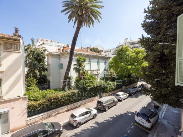 View of an old building surrounded by trees in Nice, with cars parked on the street.