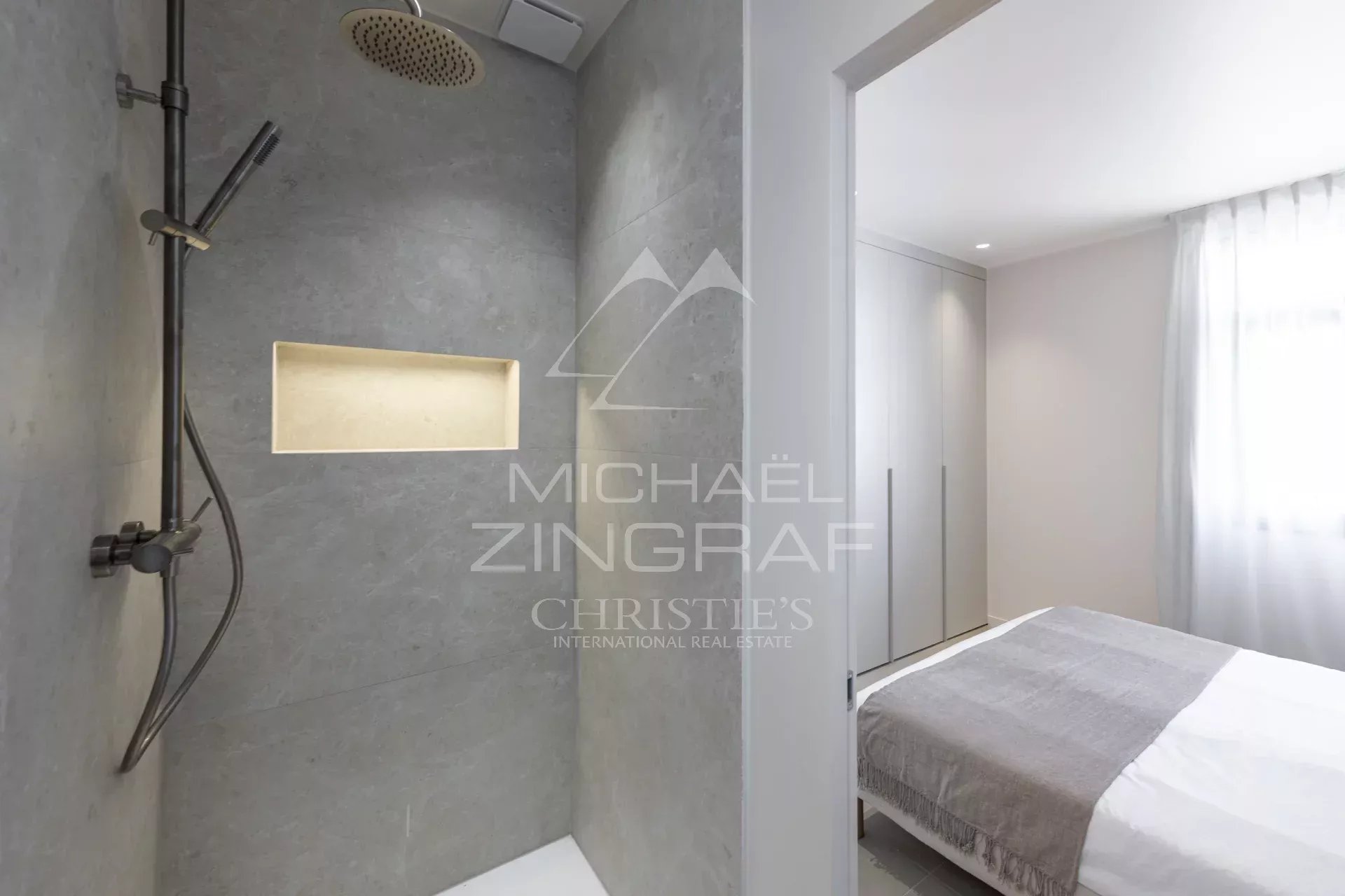 Modern bathroom with shower and adjacent bedroom in a renovated apartment.