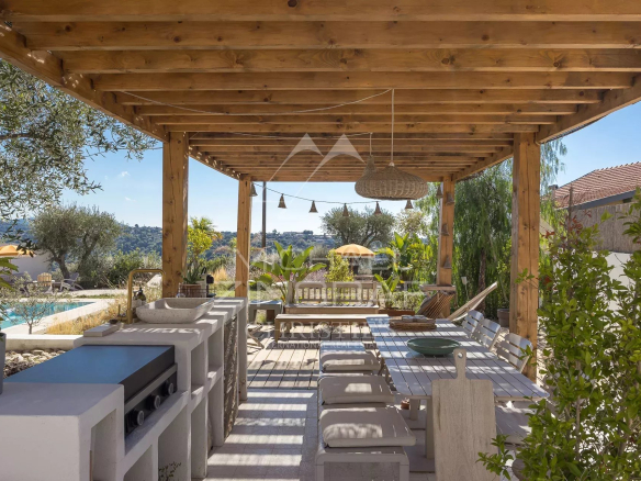 Wooden terrace with outdoor furniture and unobstructed views of nature, swimming pool in the background.