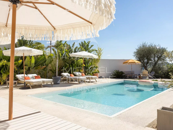 Swimming pool of a renovated villa in Nice with sun loungers and parasols, surrounded by plants.