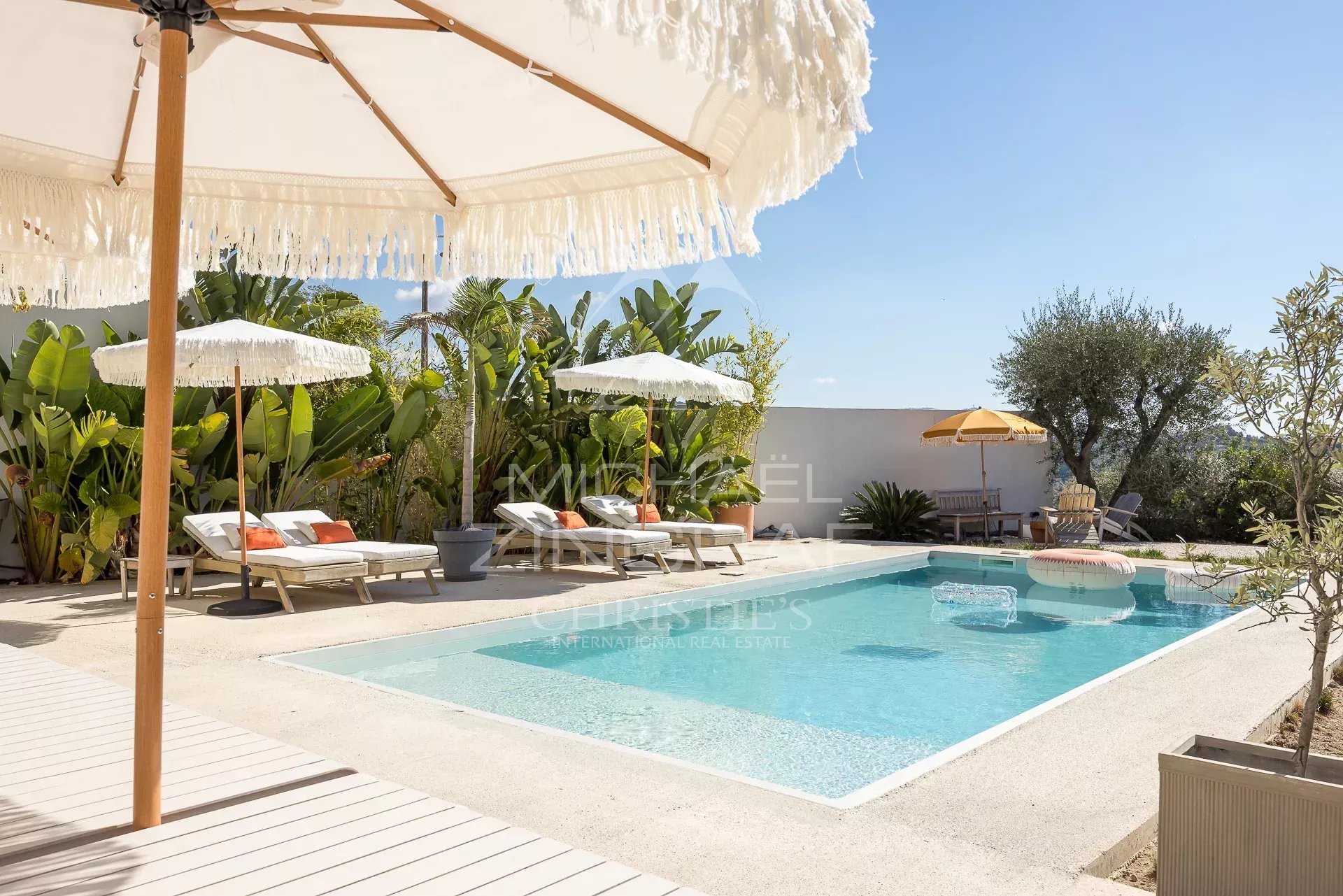 Piscine d'une villa rénovée avec chaises longues et parasols, entourée de végétation à Nice.