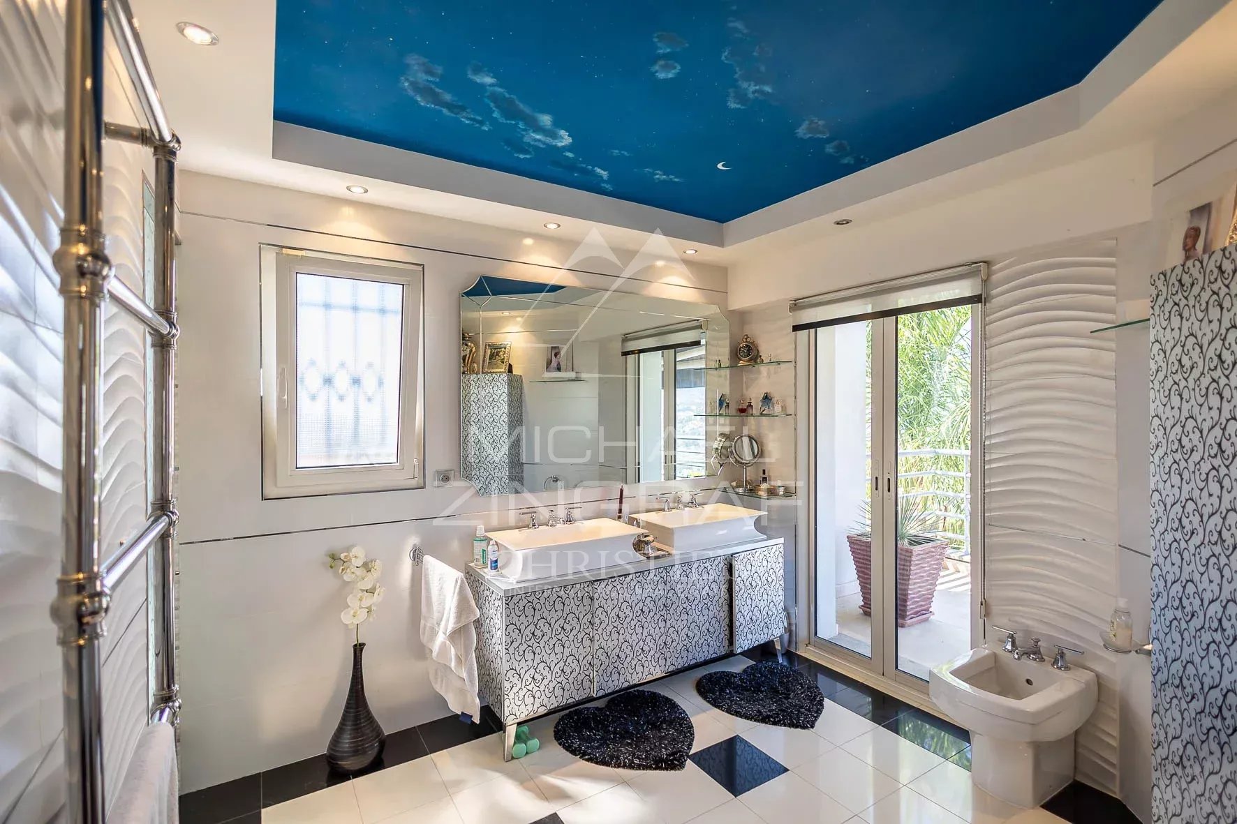 Salle de bain moderne avec un plafond bleu, baignoire et fenêtres donnant sur l'extérieur.