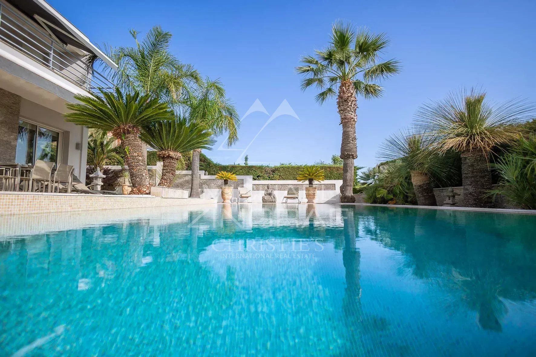 Piscine d'une villa avec palmiers et terrasses à Nice, vue dégagée sur la mer.