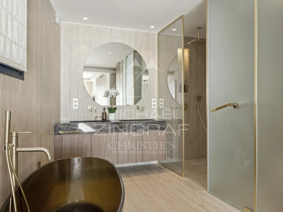 Salle de bain moderne avec baignoire dorée et miroir rond, décorée dans des tons neutres.