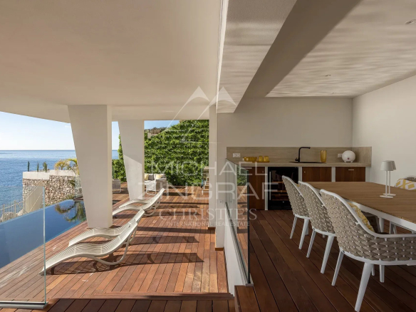 Terrasse moderne avec vue sur la mer à Nice, mobilier en bois et chaises longues.