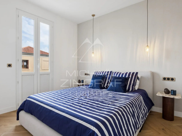 Chambre moderne avec lit à rayures bleues et blanches, fenêtres laissant entrer la lumière.