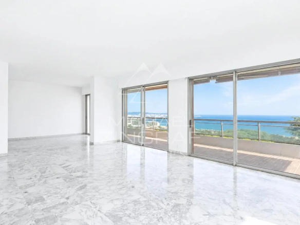 Intérieur d'un appartement spacieux avec vue sur la mer à Nice, fenêtres ouvertes sur une terrasse.