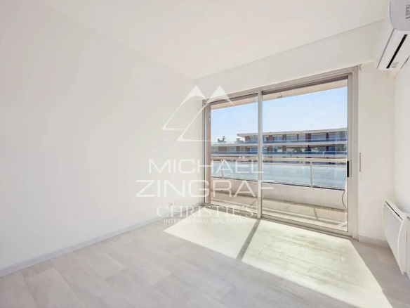 Intérieur d'un appartement lumineux avec vue sur la mer à Nice, fenêtres ouvertes sur un balcon.