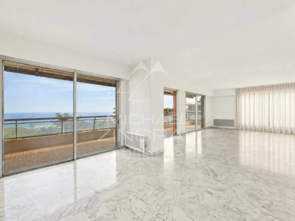 Intérieur d'un appartement spacieux avec vue sur la mer à Nice, grandes fenêtres et sol en marbre.
